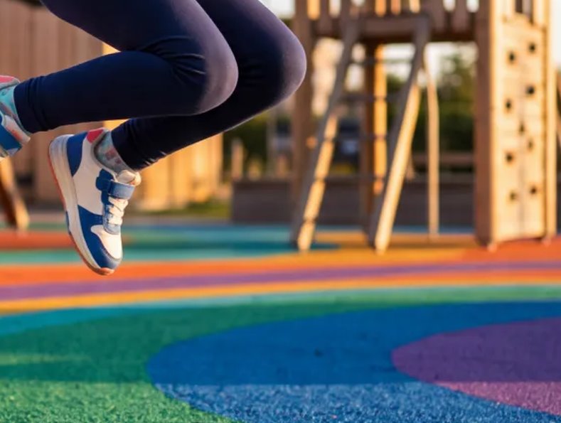 Niña saltando sobre un pavimento continuo de caucho de colores en un parque infantil